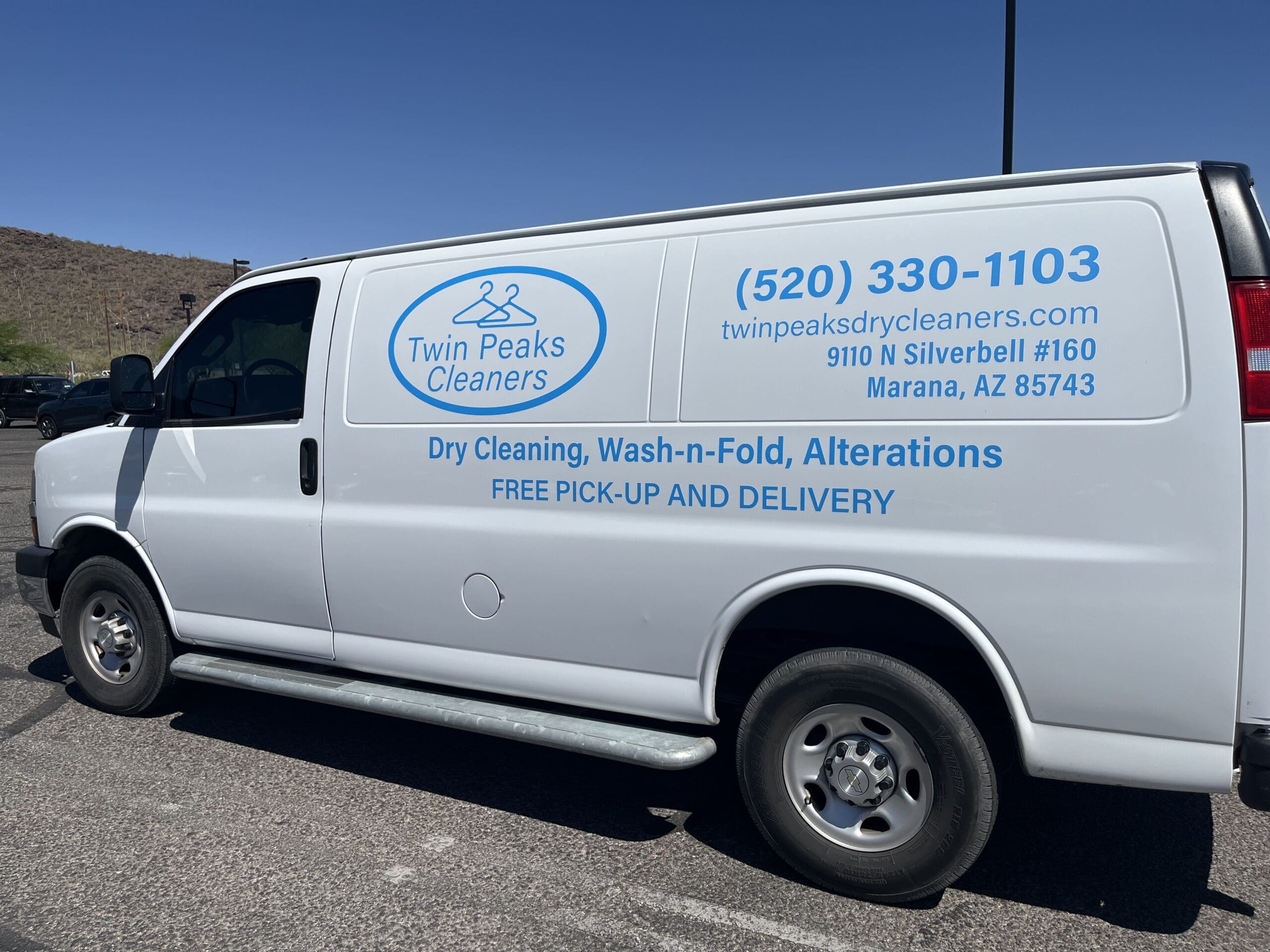 White van with "Twin Peaks Cleaners" branding, contact information, and services for dry cleaning, wash-and-fold, alterations, and free pick-up and delivery, parked in a lot.